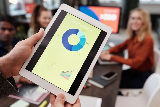 Business team reviewing digital marketing statistics on a tablet during an indoor meeting. Marketing resource management examples, taken apart