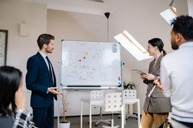 Colleagues collaborating at a business meeting, analyzing graphs on a whiteboard. Reading marketing resource management trends with a cool head